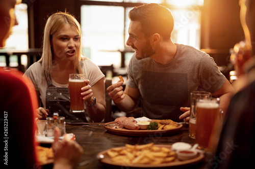 Young couple drinking beer and eating lunch with friends in a pub.