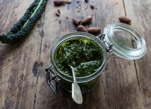 Closeup glass jar with yummy kale pesto placed on lumber tabletop near fresh peanuts photo