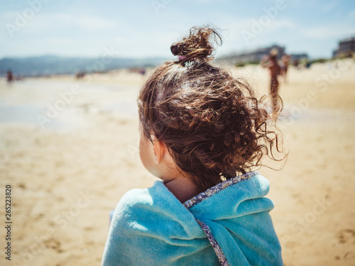 Rear view of girl wrapped in towel standing on beach photo