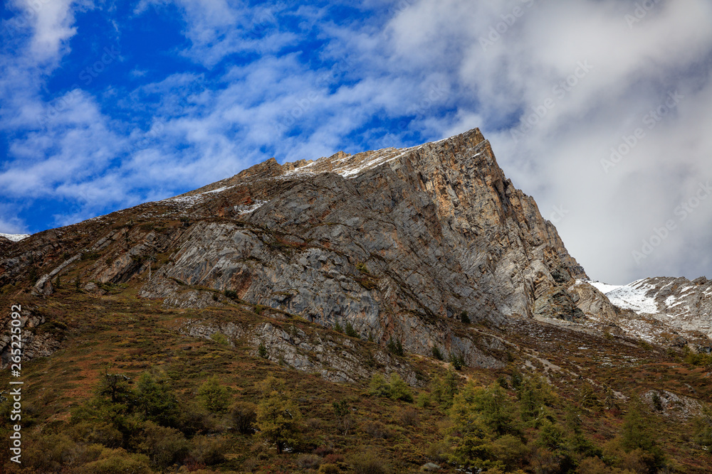 Mountain Cliff, Jagged Steep Rock Face Cliffs, extreme vertical drop, mountaineering and climbing, Blue Sky White Clouds in Background, Landscape Graphic Image.