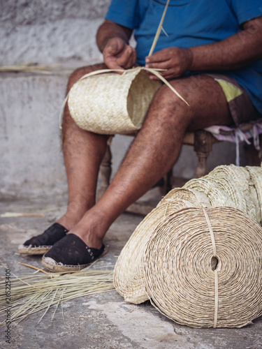 Hands of anonymous artisan showing lovely basket with floral ornament braided from dried palm fiber