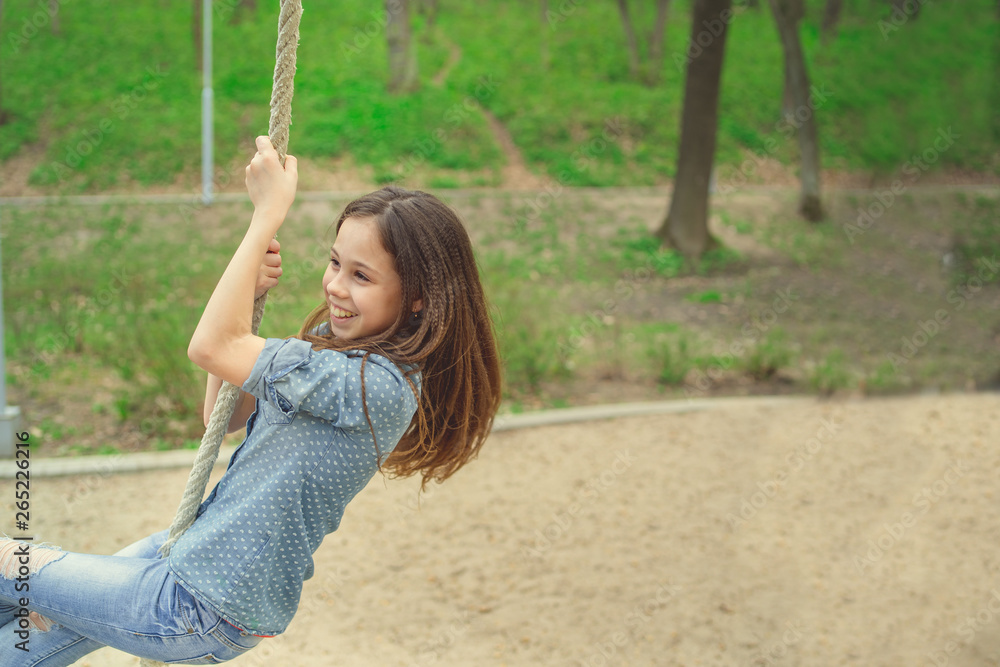 Smiling girl riding around on rope Charming cheerful brunette girl with eyes closed riding around on rope on playground in park Smiling girl riding around on rope Charming cheerful brunette girl with eyes closed riding around on rope on playground in park