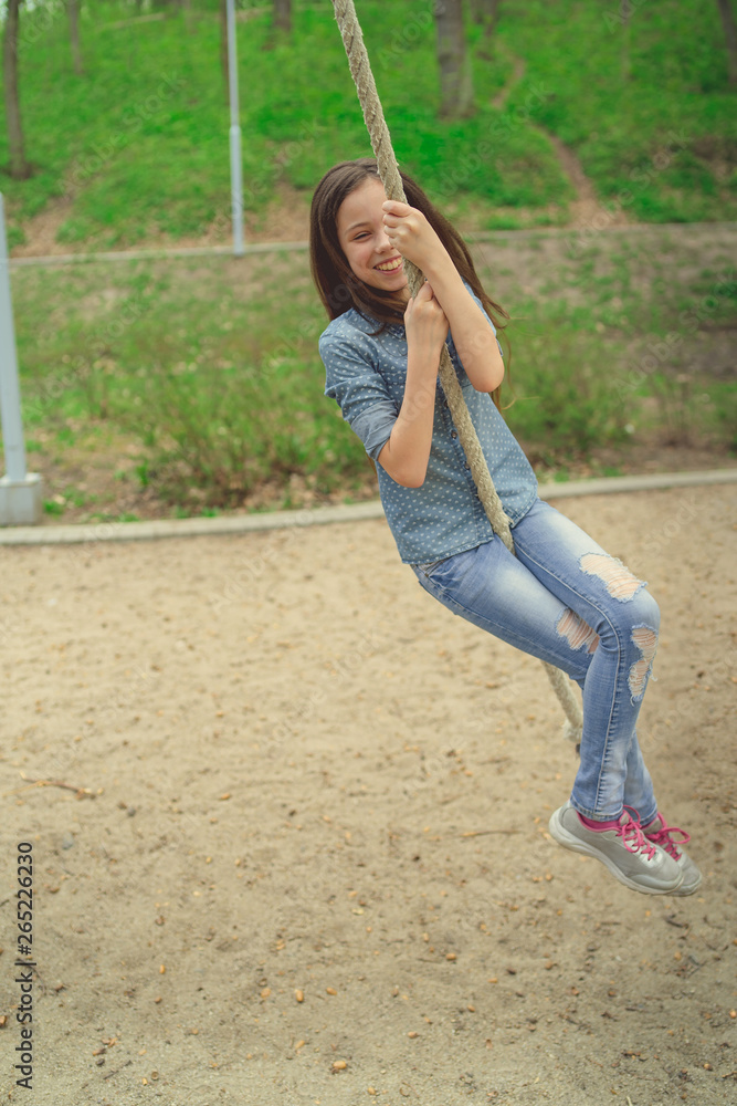 Smiling girl riding around on rope Charming cheerful brunette girl with eyes closed riding around on rope on playground in park Smiling girl riding around on rope Charming cheerful brunette girl with eyes closed riding around on rope on playground in park
