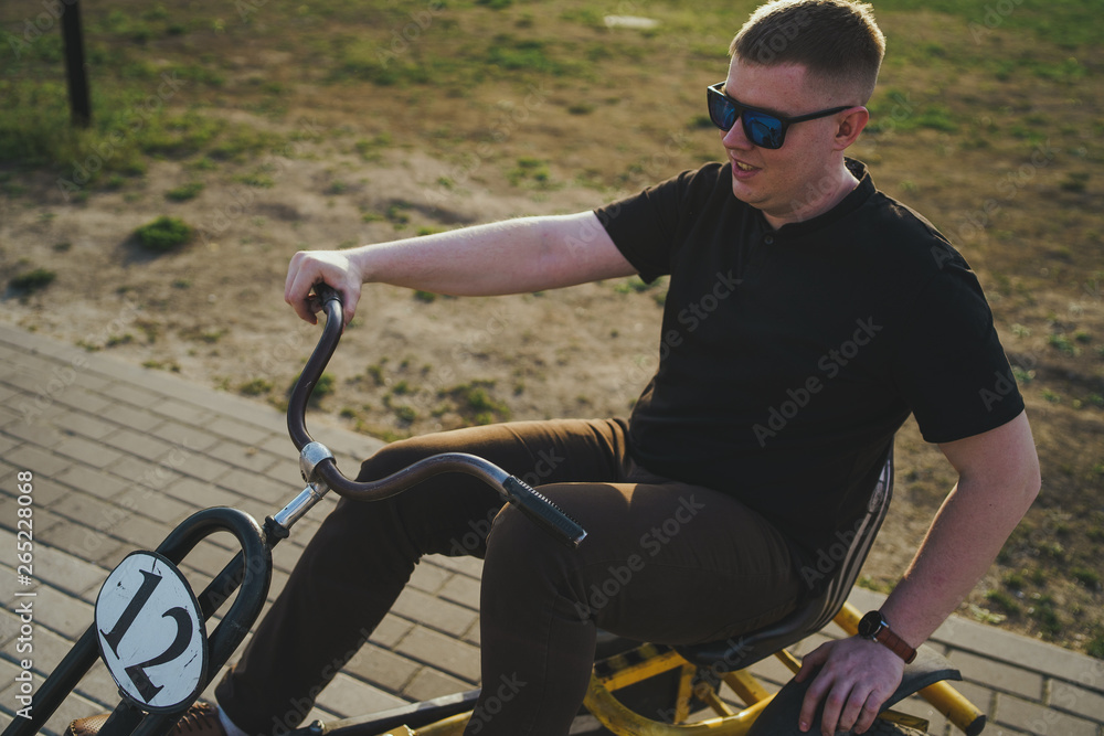 Obraz premium Man sitting on bicycle on road Male in sunglasses riding retro bike on sidewalk in park on sunny day
