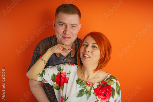 Couple of lovers on an orange background. The husband and wife, the concept of family. Young man and woman with bright red hair