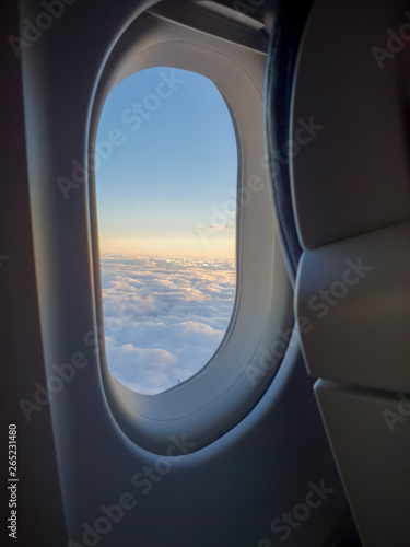 The view outside an airplane window with the sun setting and the clouds in the background
