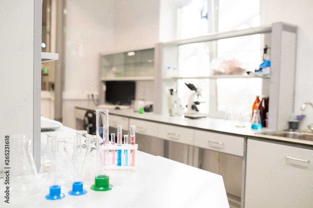 Colorful liquids in test tubes, empty beakers and stands placed on table in university laboratory