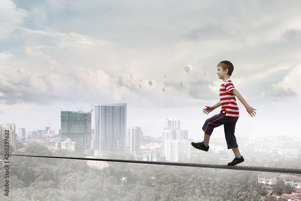 Cute joyful little boy walking on a rope over city. Mixed media Cute joyful little boy walking on a rope over city. Mixed media