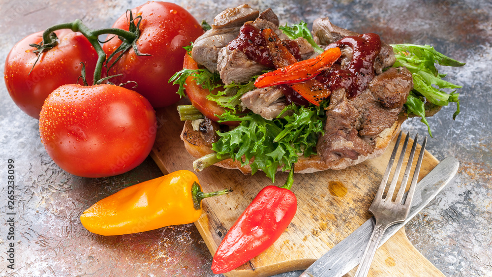 Close Up grilled meat on a traditional chabbata with sweet peppers, tomatoes and herbs on a cutting board.