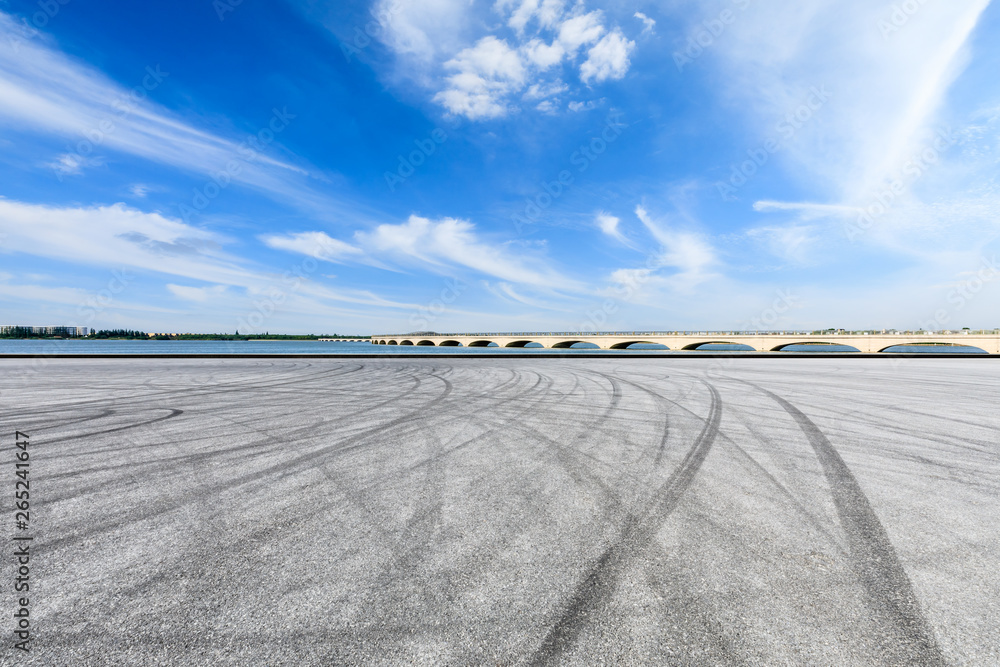 Asphalt race track ground and lake with bridge under blue sky