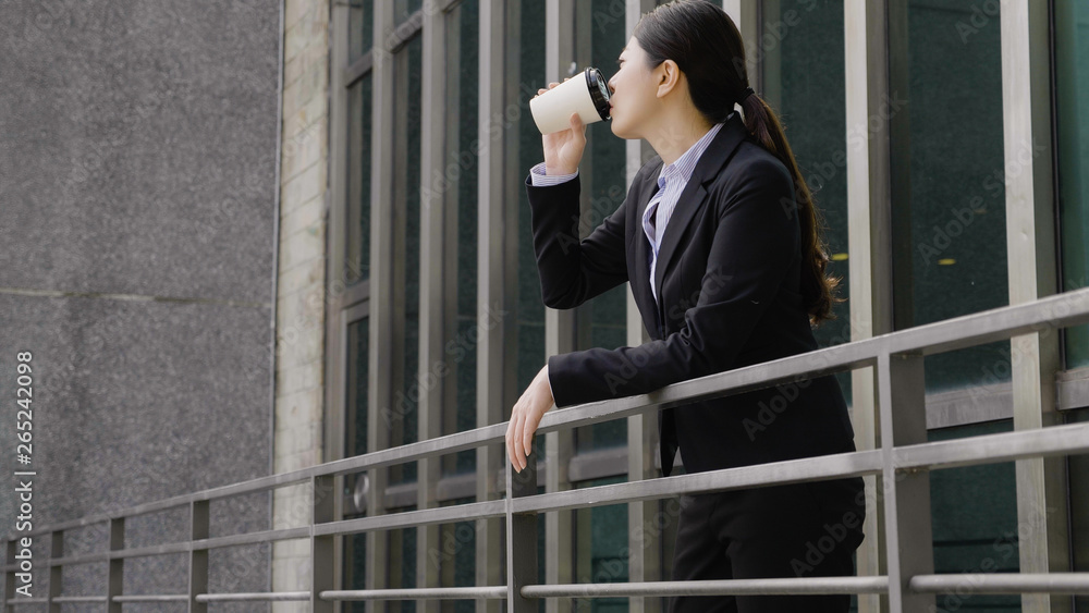 elegant asian businesswoman leaning on balcony railings outdoor drinking coffee having break. young female manager angry with employee relax calm down out modern office building. genuine lifestyle