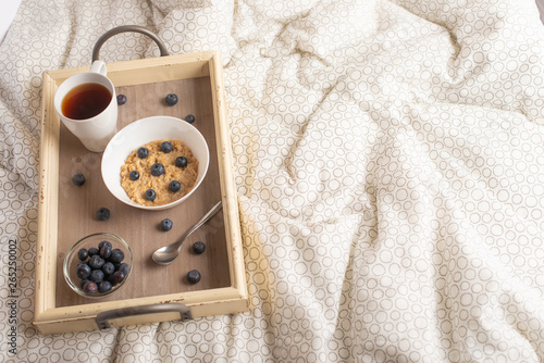 Oatmeal with berries on a tray in bed with tea, morning breakfast and mood. flat lay. good and warm