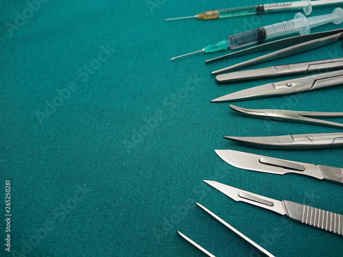 Surgical instrument, scalpel, tweezers, scissors, with liquid parenteral products in syringe on surgical green drape fabric.