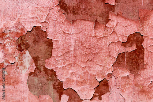 Old weathered peeling red coral paint on the wall. background texture of dirty peeled plaster wall