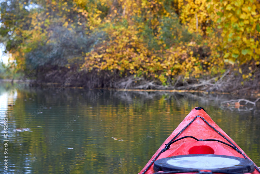 Fototapeta premium Bow of red kayak on river at calm autumn day. View on river from the bow of kayak. Autumn kayaking
