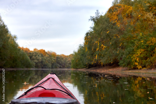Red kayak sailing down a river on a sunny autumn day against yellow foliage trees reflected in the water © watcherfox