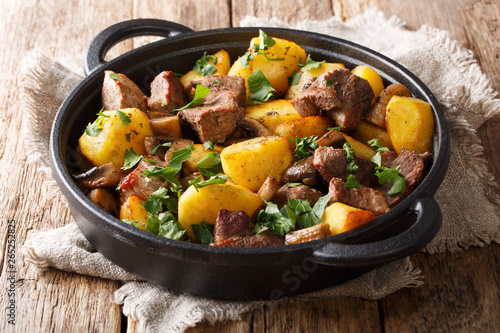 Simple hearty meal of fried potatoes with pork meat and mushrooms close-up in a pan. horizontal
