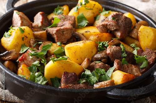 The main dish of fried pork with potatoes and mushrooms close-up in the pan. horizontal