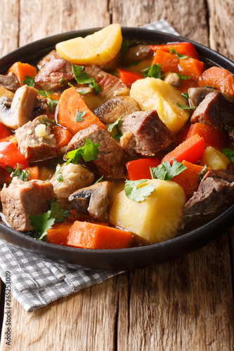pork stew with mushrooms, potatoes, carrots and peppers close-up on a plate. vertical