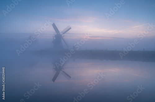 Windmill 'de Witte Molen' reflected in the canal during a foggy dawn in Holland.