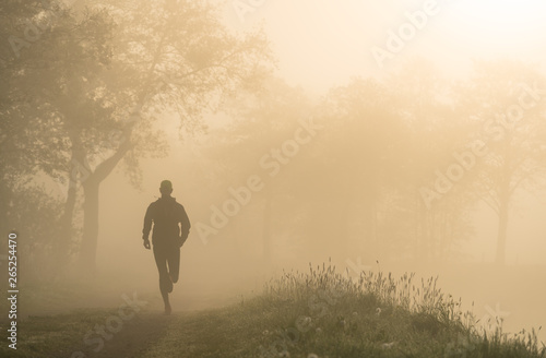 Athlete running on a gravel road during a foggy, spring sunrise in the countryside. © sanderstock