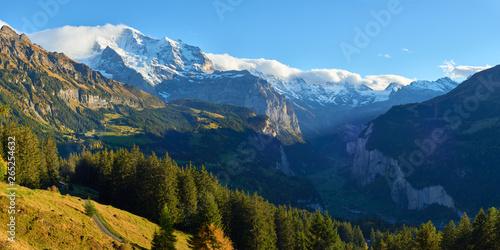 Panoramic view of the Jungfrau high mountain peak in the clouds and Lauterbrunnen valley near Swiss Alpine village Wengen at sunset.