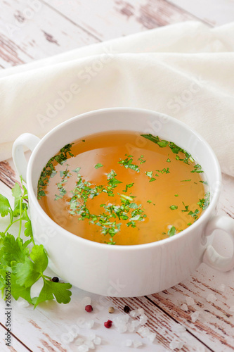 Cooked hot bone broth with spices and fresh herbs. Medical dietary broth and superfood. For ketogenic diet and paleo diet. Serve on an individual plate on a wooden background and with a white napkin.