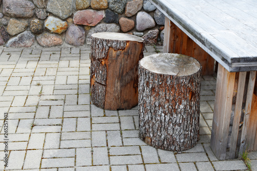 Cut trunk of tree as bench and part of picnic table on pavement and rock wall background outdoors in spring day.