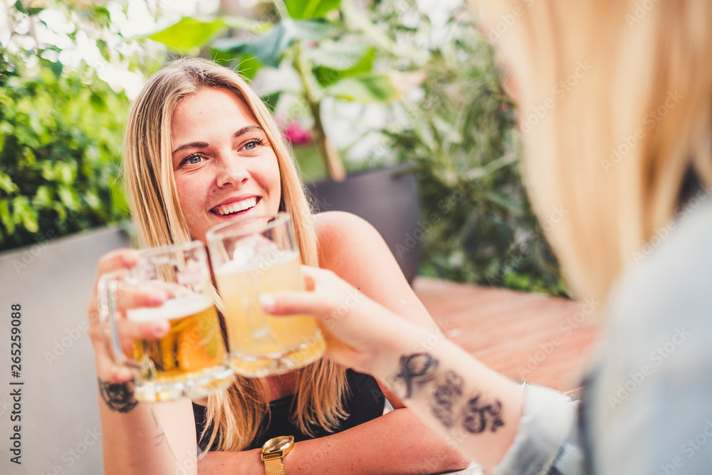 Cheerful blonde with friend at the bar drinking beer and celebrating in friendship toasting the glasses and having fun together - happy people celebrate with friends Cheerful blonde with friend at the bar drinking beer and celebrating in friendship toasting the glasses and having fun together - happy people celebrate with friends