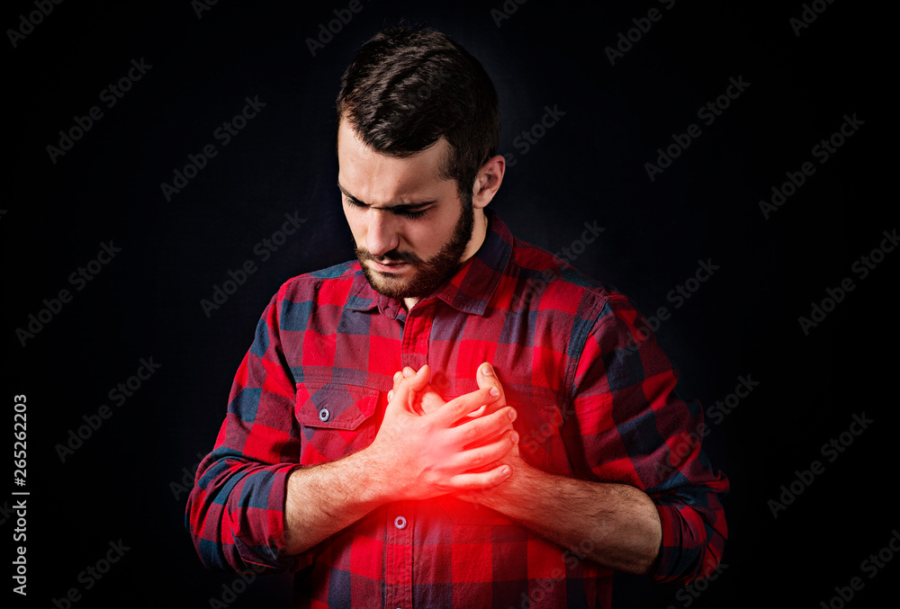 pain in the heart region of a young man with a beard on a black background pain in the heart region of a young man with a beard on a black background