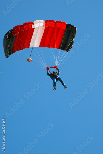 Figure of a parachutist with a bright parachute against a blue sky.