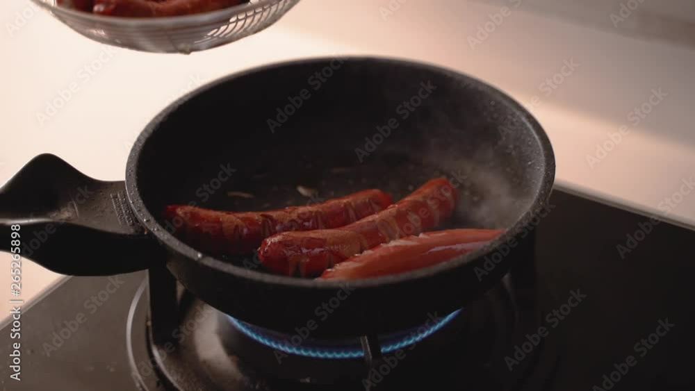 Hands of chef cooking sausages with tongs in hot frying pan on gas stove Hands of chef cooking sausages with tongs in hot frying pan on gas stove