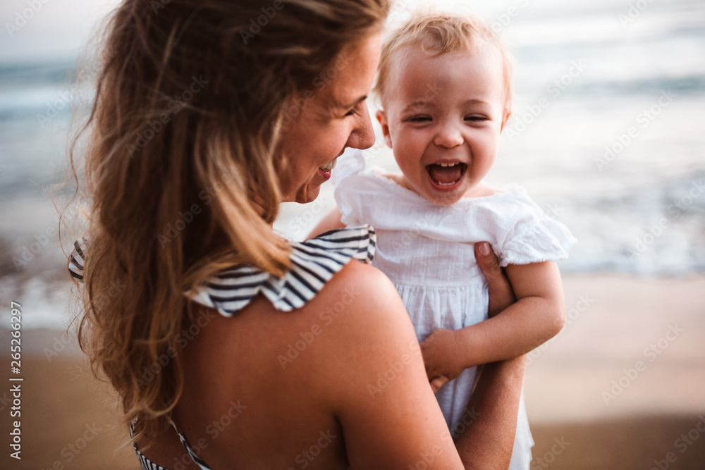 Close-up of young mother with a toddler girl on beach on summer holiday. - obrazy, fototapety, plakaty 