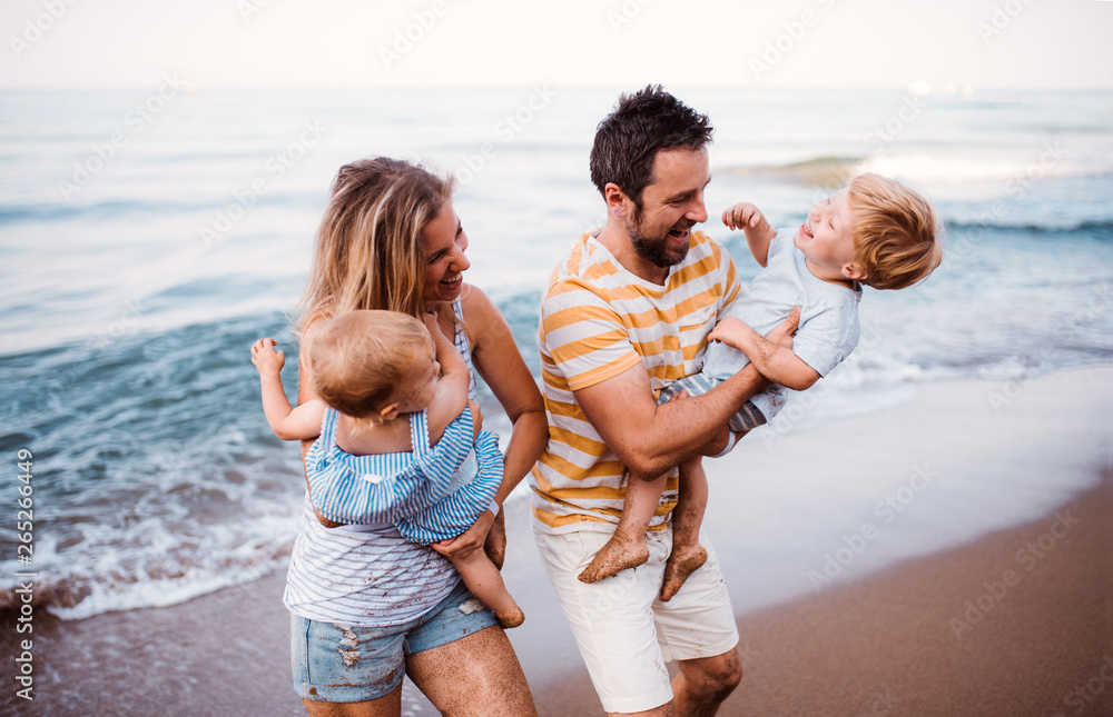 A young family with two toddler children walking on beach on summer holiday.