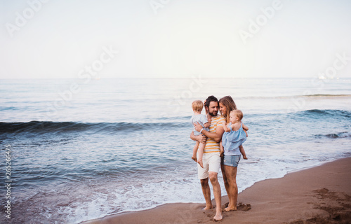 A young family with two toddler children standing on beach on summer holiday.