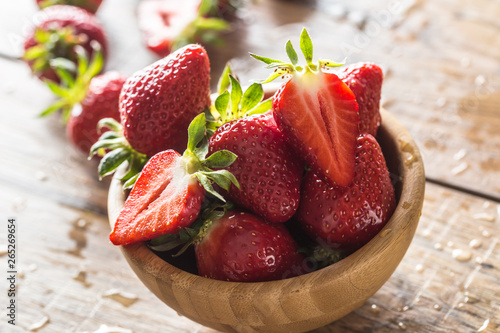 Juicy washed strawberries in wooden bowl on kitchen table