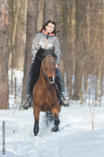 A woman in warm jacket riding a brown horse in the forest
