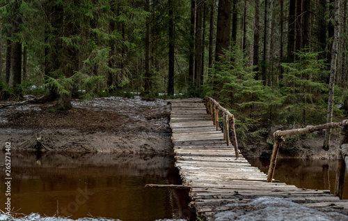 Old wooden bridge over the river in the forest. The ground is covered with a thin layer of snow. Forest in early spring