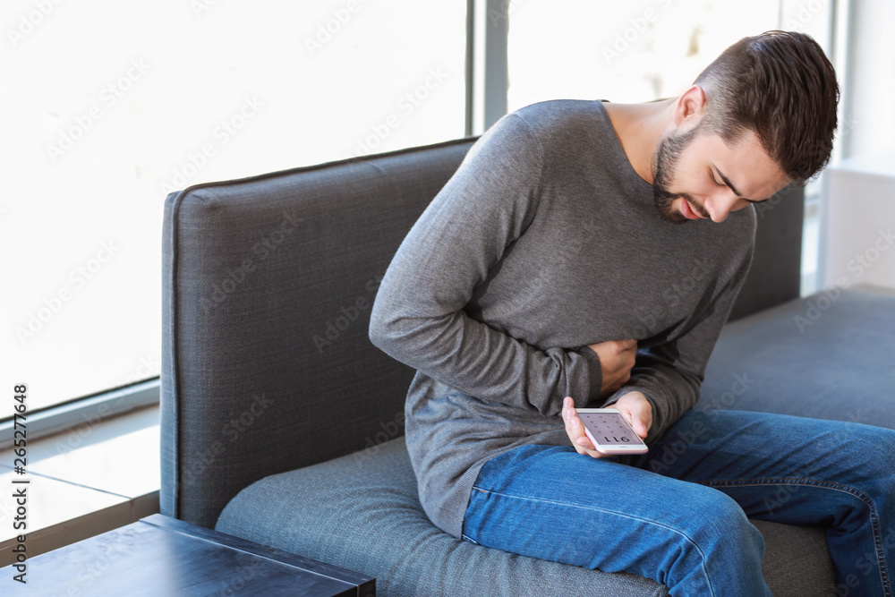 Young man calling an ambulance while suffering from stomachache at home