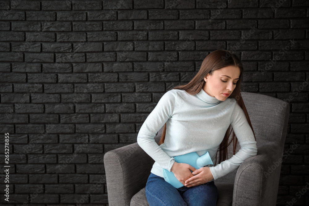 Woman suffering from abdominal pain while sitting in armchair Woman suffering from abdominal pain while sitting in armchair