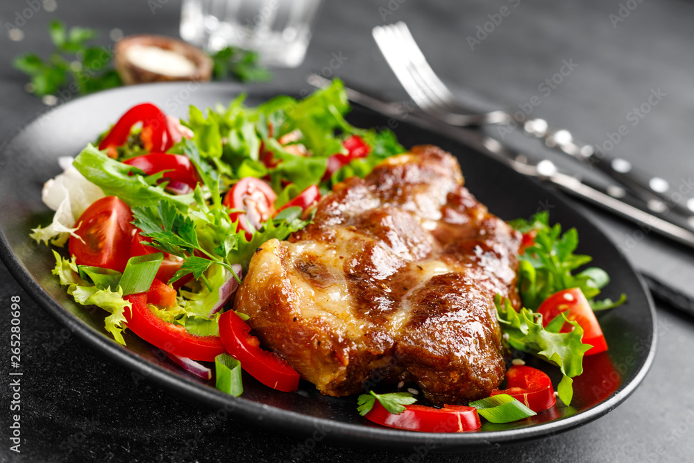 Baked pork steak with fresh vegetable salad on a plate Baked pork steak with fresh vegetable salad on a plate