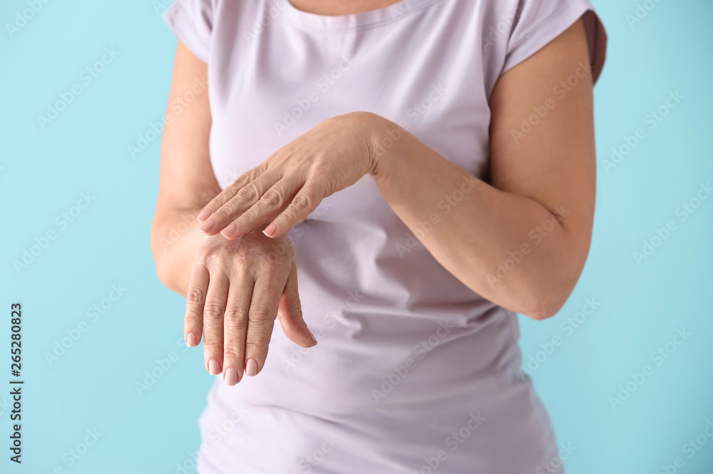 Mature woman applying hand cream on color background Mature woman applying hand cream on color background