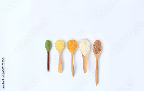Various colorful powder in different wooden spoons isolated on white background.