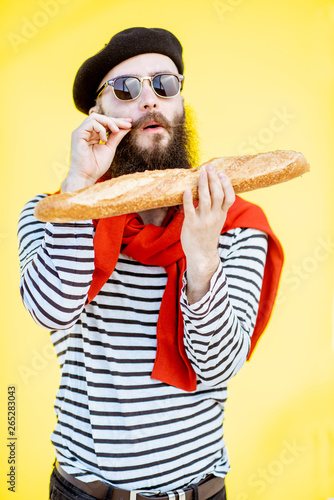 Portrait of a stylish man dressed in french style with striped shirt, hat and red scarf on the yellow background