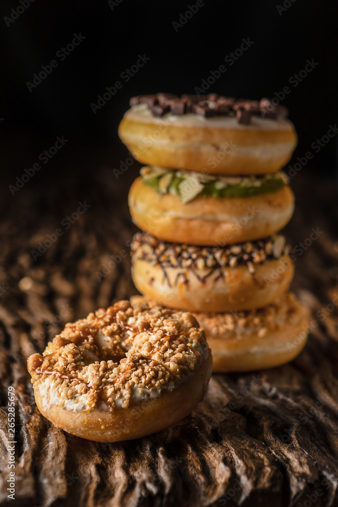 food background of a piece of donut on wooden plank with a stack of donuts behind on dark background