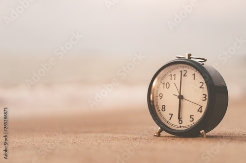 Clock on sand beach with smooth wave background.