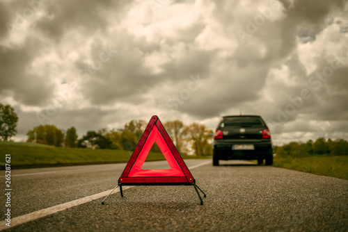 A warning triangle in front of a car with a breakdown on a side strip