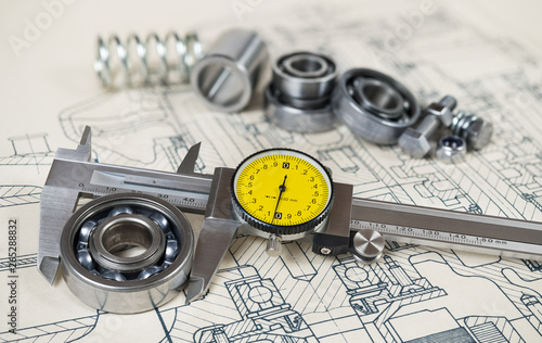 Accurate caliper gauge. Ball bearings diameter. Technical drafting. Analog metal measuring instrument with yellow round dial. Group of steel components on document. Machining concept. Selective focus.