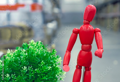 Red wooden doll Gestalta next to a green plant. photo