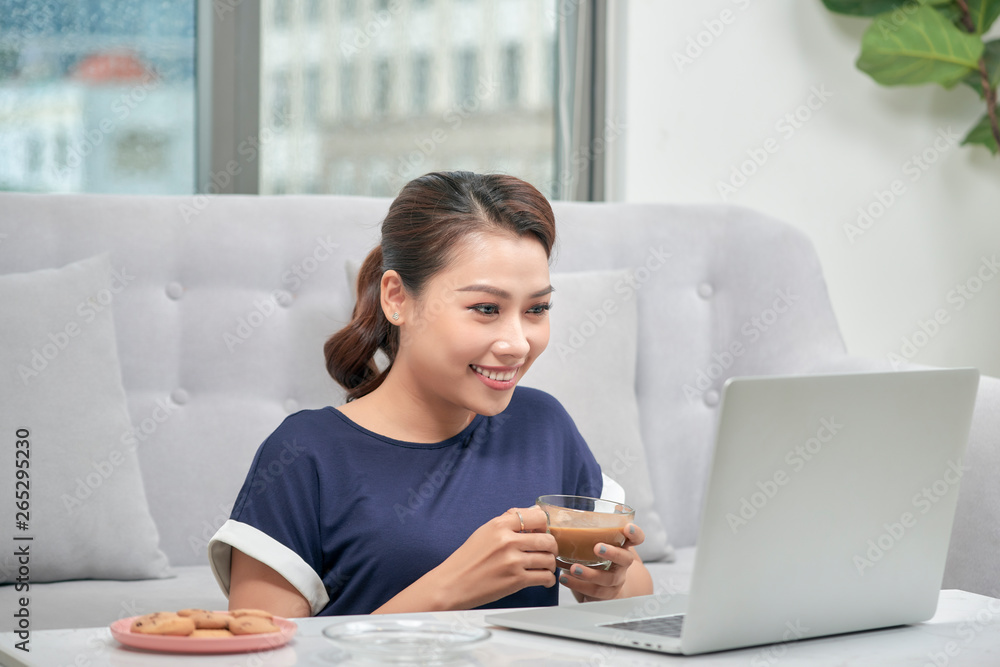 Smiling young asian woman holding cup of coffee while sitting on the floor with laptop computer and credit card at home Smiling young asian woman holding cup of coffee while sitting on the floor with laptop computer and credit card at home